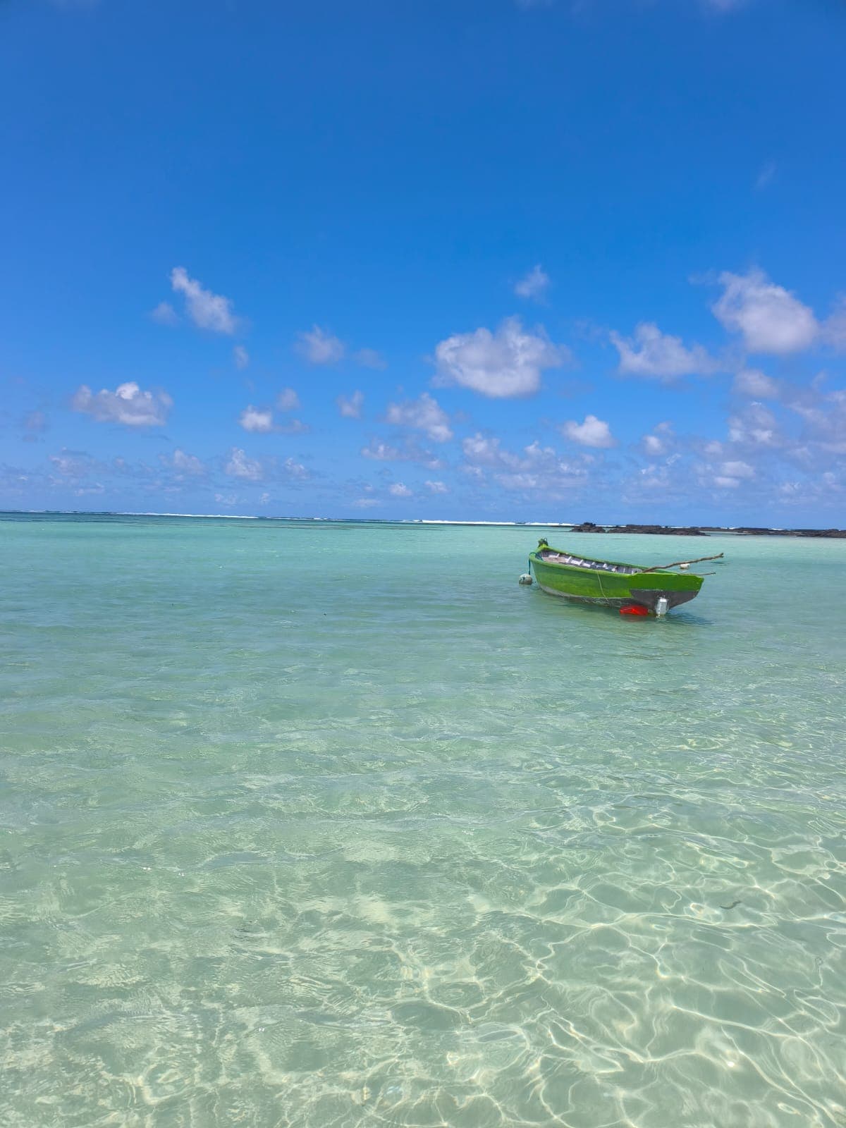 Barque verte sur une eau turquoise limpide sous un ciel bleu parsemé de nuages blancs.