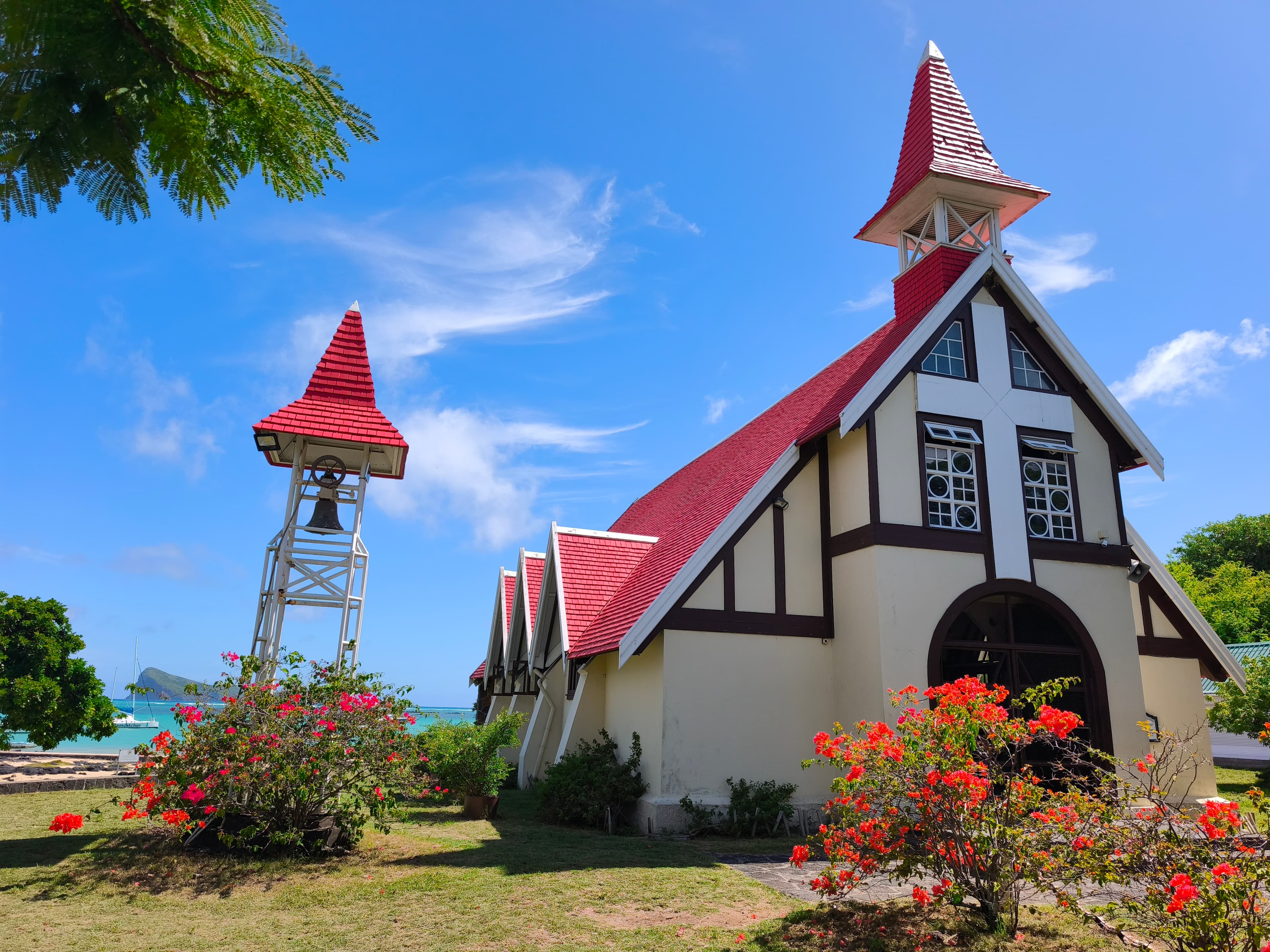 Église au toit rouge et clocher blanc avec bougainvilliers sous un ciel bleu éclatant.