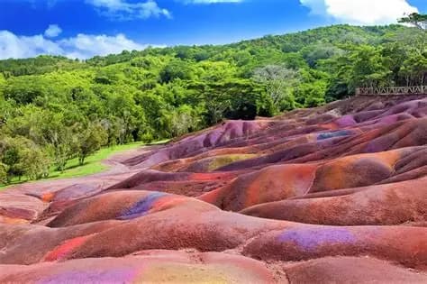 Dunes de sable multicolores de Chamarel entourées d'une forêt verdoyante sous un ciel bleu.